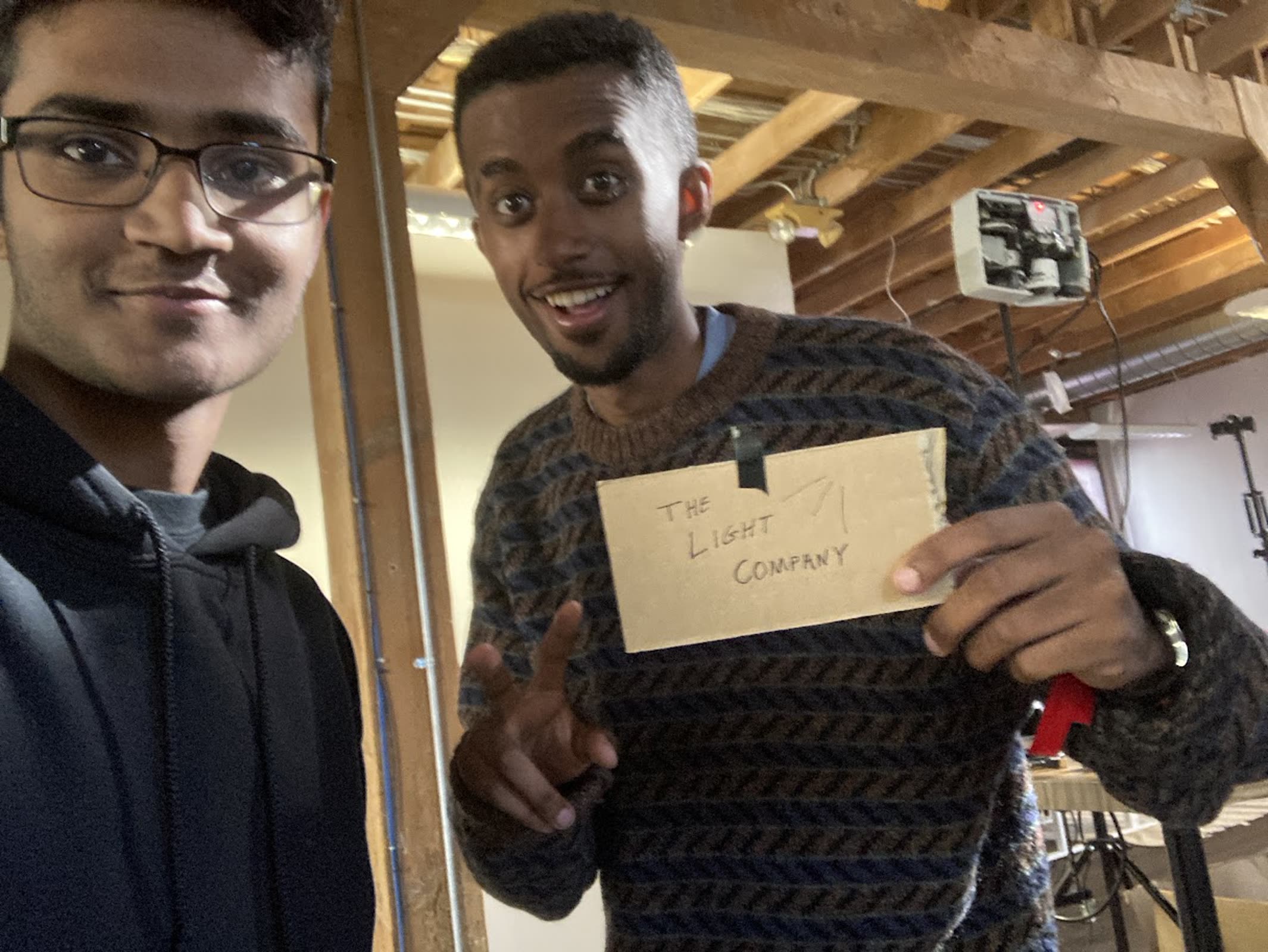 The two founders, one holding a handwritten The Light Company sign, with their hardware behind them.