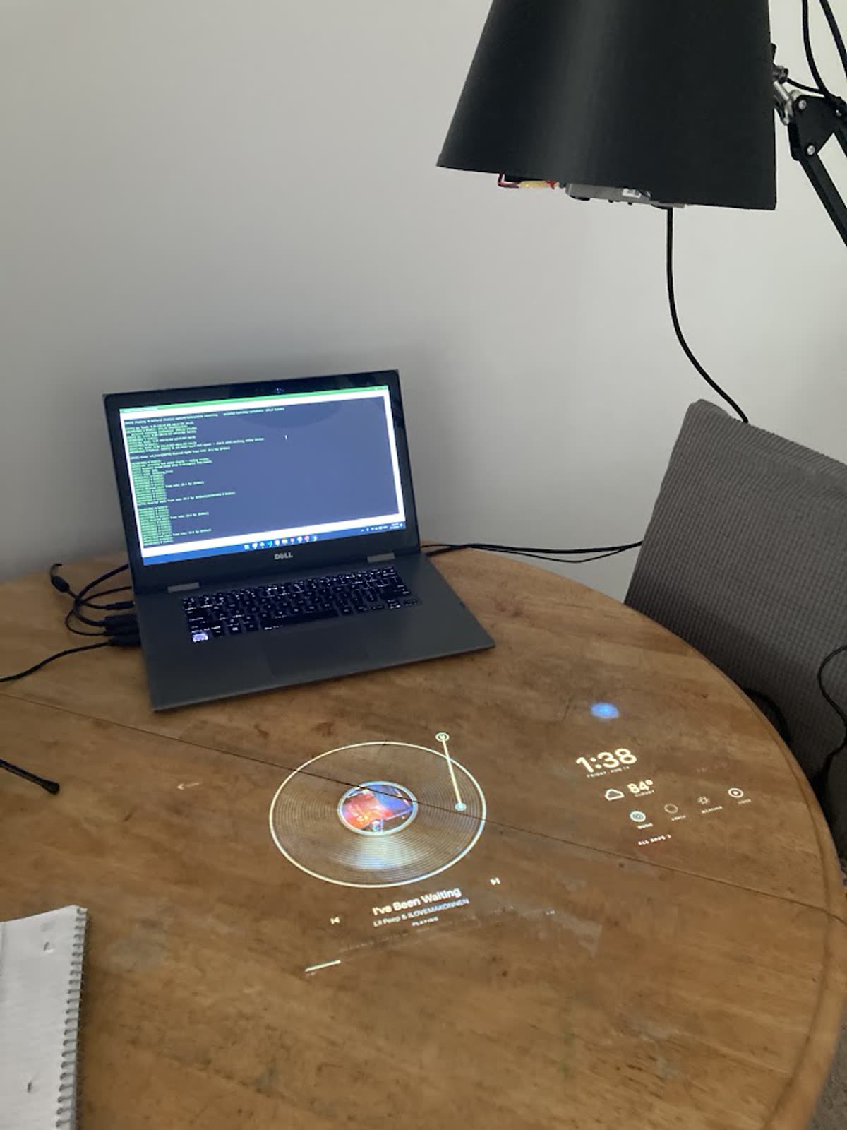 A Prism lamp above a wooden table with projected music, weather, and clock interfaces.